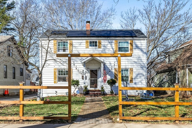 view of front of property featuring solar panels, a fenced front yard, and a chimney