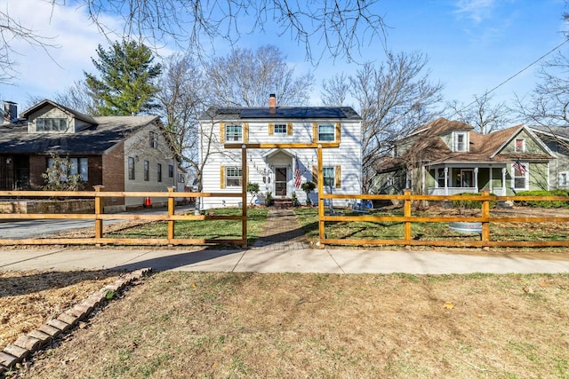 view of front of house featuring a fenced front yard, solar panels, and a chimney