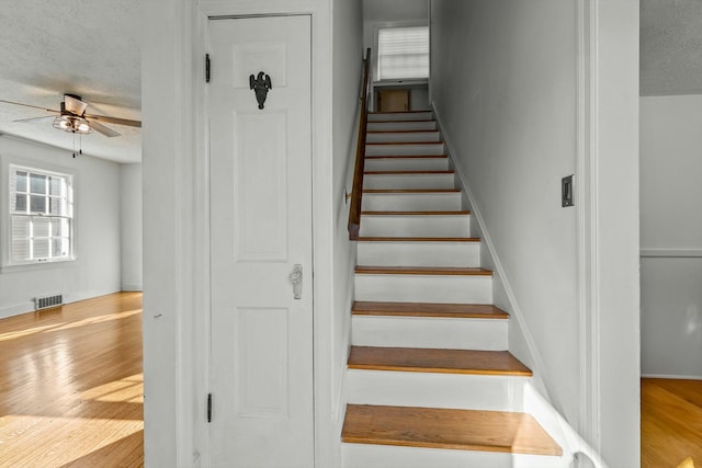 staircase featuring visible vents, a textured ceiling, wood finished floors, and a ceiling fan