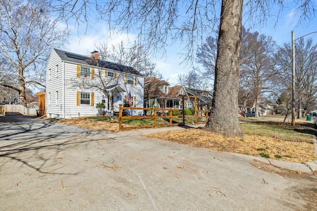 view of front of home with fence, driveway, roof mounted solar panels, and a chimney