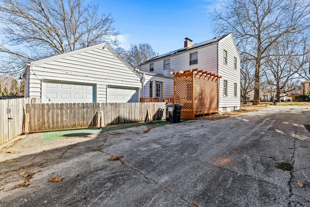 back of house featuring roof mounted solar panels, a chimney, and fence