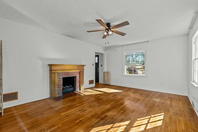 unfurnished living room with visible vents, a brick fireplace, a textured ceiling, a ceiling fan, and wood-type flooring