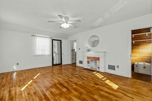 unfurnished living room featuring a brick fireplace, a ceiling fan, visible vents, and wood-type flooring