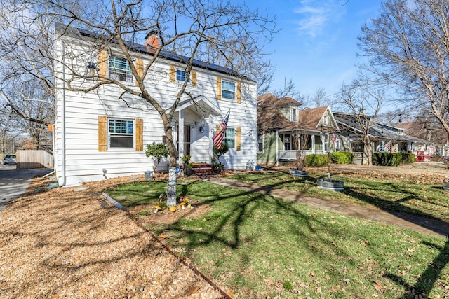 colonial house featuring roof mounted solar panels, a chimney, and a front yard