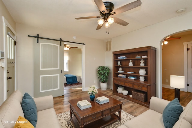 living room featuring a ceiling fan, visible vents, arched walkways, light wood-style floors, and a barn door