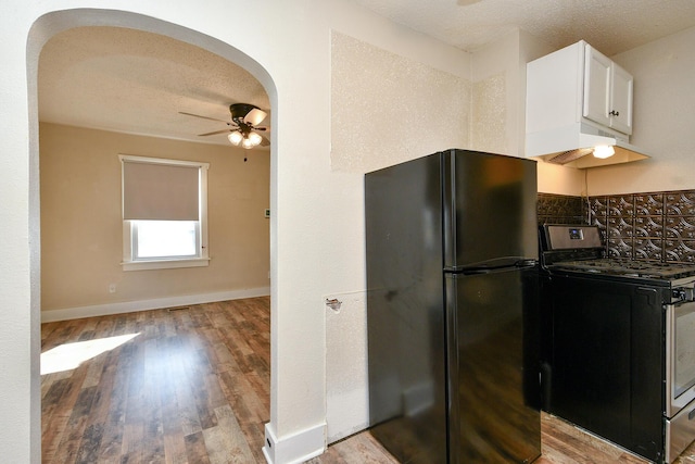 kitchen featuring gas stove, arched walkways, freestanding refrigerator, ceiling fan, and under cabinet range hood