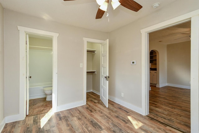 unfurnished bedroom with ceiling fan, wood finished floors, arched walkways, and baseboards