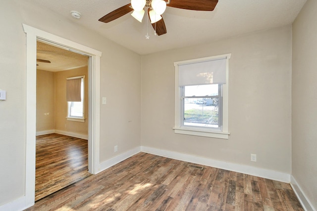 empty room with a ceiling fan, wood finished floors, baseboards, and a wealth of natural light