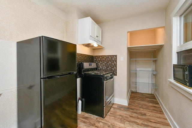 kitchen featuring under cabinet range hood, freestanding refrigerator, white cabinets, light wood finished floors, and stainless steel range with gas stovetop