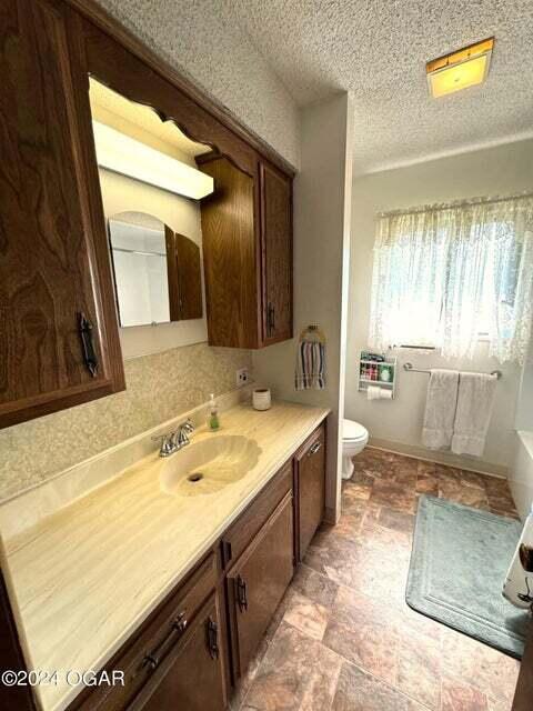 bathroom with vanity, a textured ceiling, a tub to relax in, stone finish flooring, and toilet