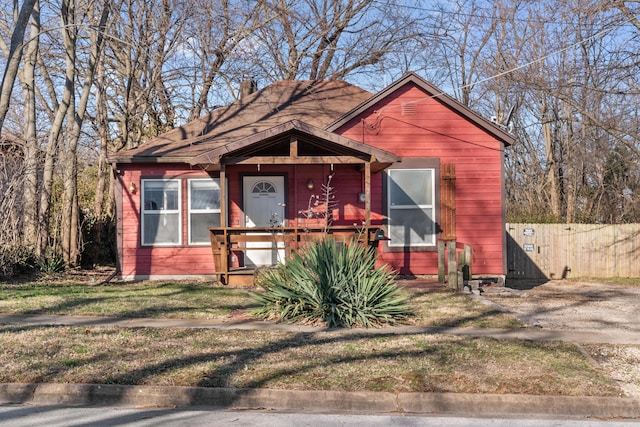 bungalow-style home with covered porch, a chimney, and fence