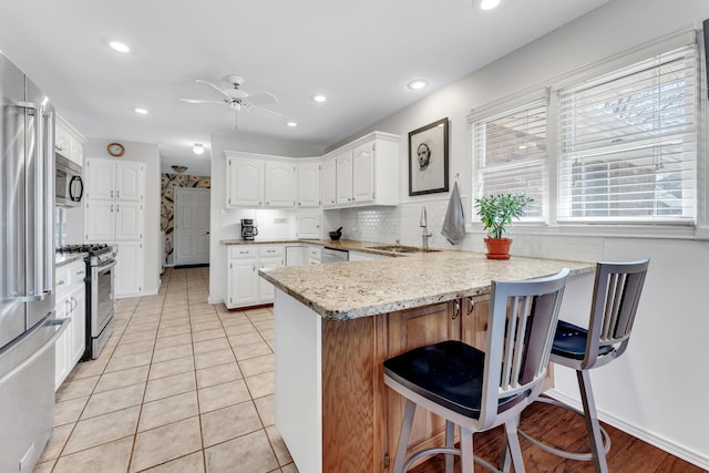 kitchen featuring a peninsula, ceiling fan, a sink, white cabinets, and appliances with stainless steel finishes