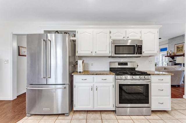 kitchen featuring light tile patterned floors, stone counters, white cabinets, and appliances with stainless steel finishes