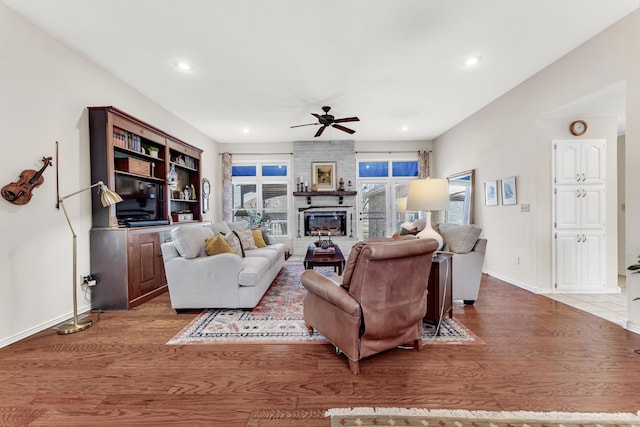 living room featuring a fireplace, baseboards, ceiling fan, and wood finished floors