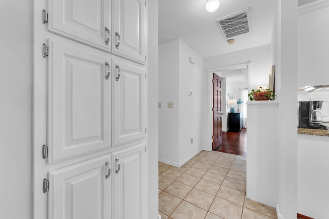 hallway with light tile patterned floors, visible vents, and baseboards