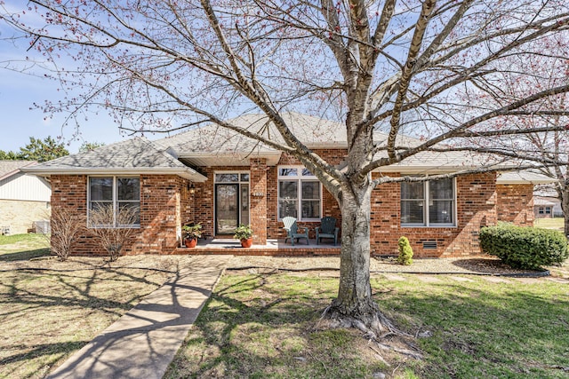 single story home with brick siding, a patio, a shingled roof, and a front yard