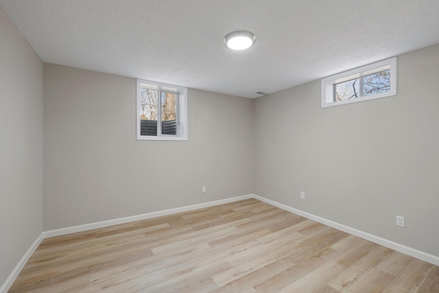 basement featuring baseboards, light wood-style floors, and a textured ceiling