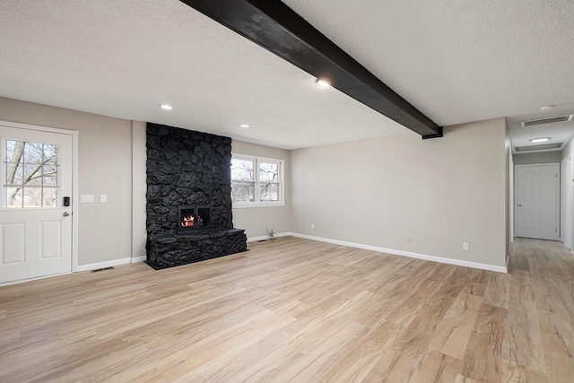 unfurnished living room with visible vents, baseboards, beam ceiling, light wood-style flooring, and a textured ceiling