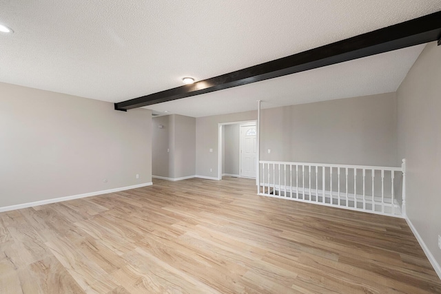 empty room with beamed ceiling, light wood-style flooring, a textured ceiling, and baseboards