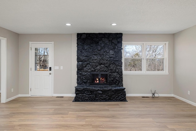 living room featuring a stone fireplace, a textured ceiling, baseboards, and light wood-style floors