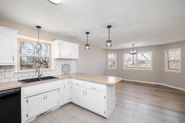 kitchen with a sink, tasteful backsplash, black dishwasher, a peninsula, and light countertops