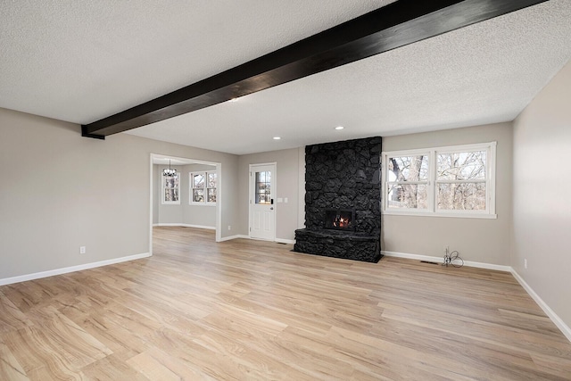 unfurnished living room featuring baseboards, beam ceiling, a textured ceiling, and light wood finished floors