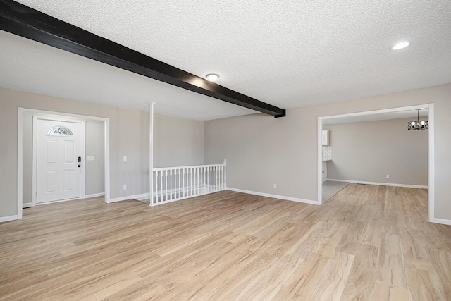 unfurnished room featuring beam ceiling, light wood-style flooring, and a textured ceiling