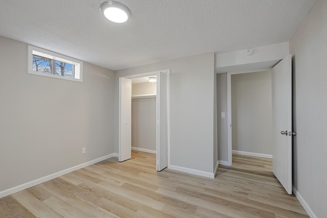 unfurnished bedroom with a textured ceiling, light wood-type flooring, and baseboards