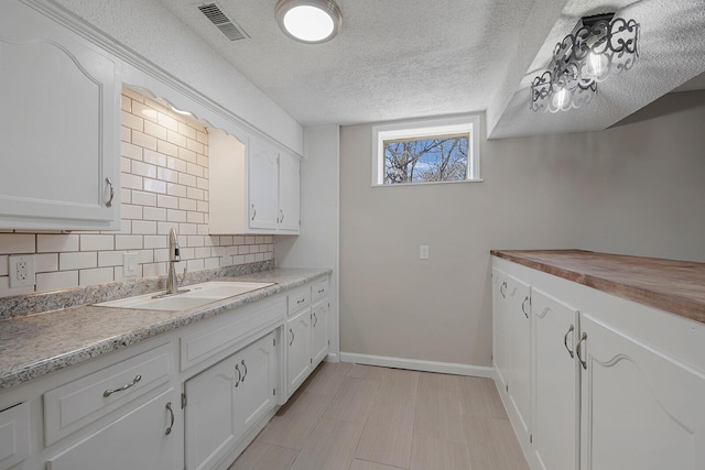 kitchen with visible vents, white cabinetry, decorative backsplash, a textured ceiling, and a sink