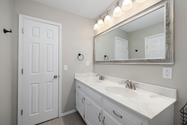 bathroom with double vanity, a textured ceiling, baseboards, and a sink