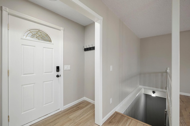 foyer entrance with a textured ceiling, baseboards, and wood finished floors