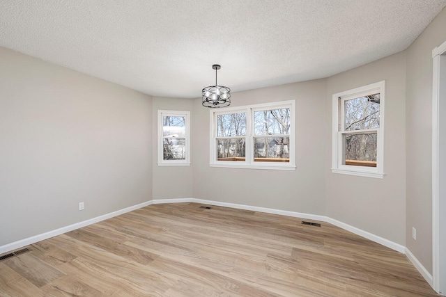 empty room featuring visible vents, baseboards, an inviting chandelier, and light wood finished floors