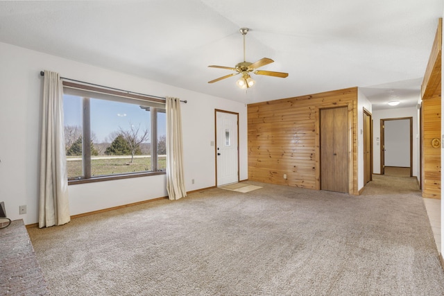 unfurnished living room with wooden walls, carpet, and a ceiling fan