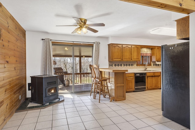 kitchen featuring brown cabinets, black appliances, wood walls, light countertops, and ceiling fan