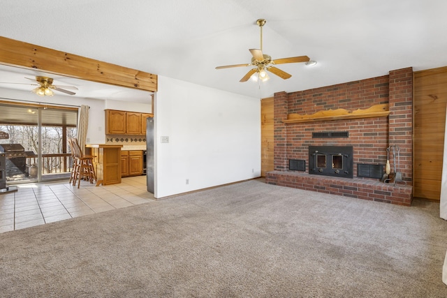 unfurnished living room with wooden walls, a ceiling fan, light tile patterned flooring, a fireplace, and light colored carpet