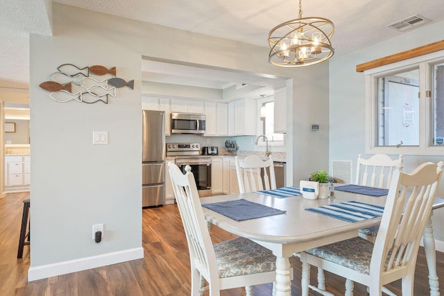 dining space with an inviting chandelier, wood finished floors, visible vents, and baseboards