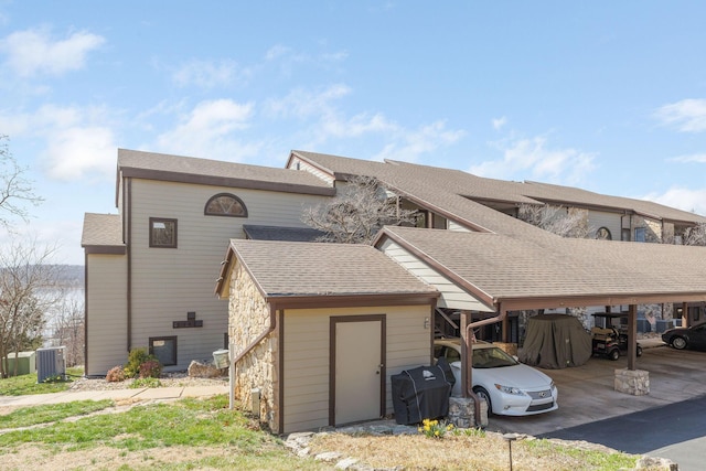 rear view of house featuring an outbuilding, stone siding, a shed, cooling unit, and a shingled roof