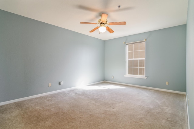 carpeted spare room featuring baseboards and a ceiling fan