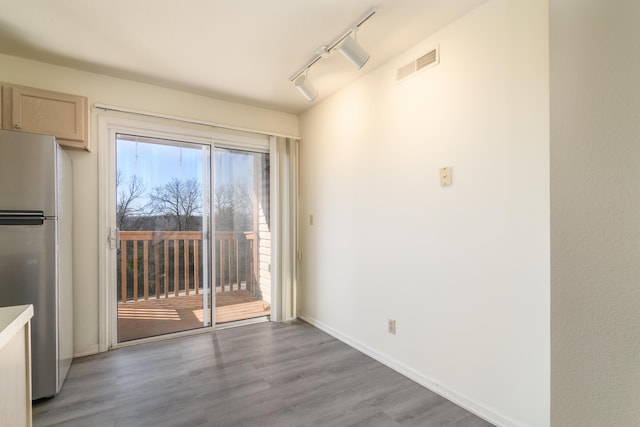 empty room featuring rail lighting, wood finished floors, visible vents, and baseboards