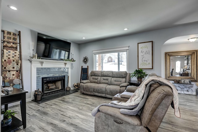 living area featuring arched walkways, recessed lighting, a fireplace with raised hearth, and wood finished floors