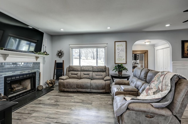 living room with recessed lighting, arched walkways, wood finished floors, and a tiled fireplace