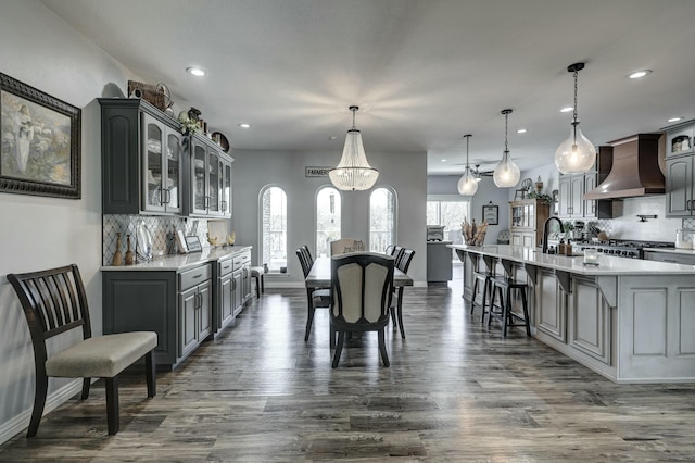 kitchen with a sink, glass insert cabinets, light countertops, custom range hood, and dark wood-style flooring