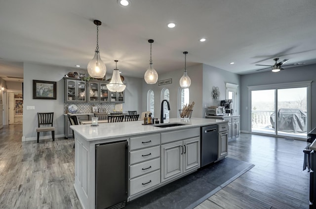 kitchen with an island with sink, a sink, light countertops, dishwasher, and light wood-type flooring