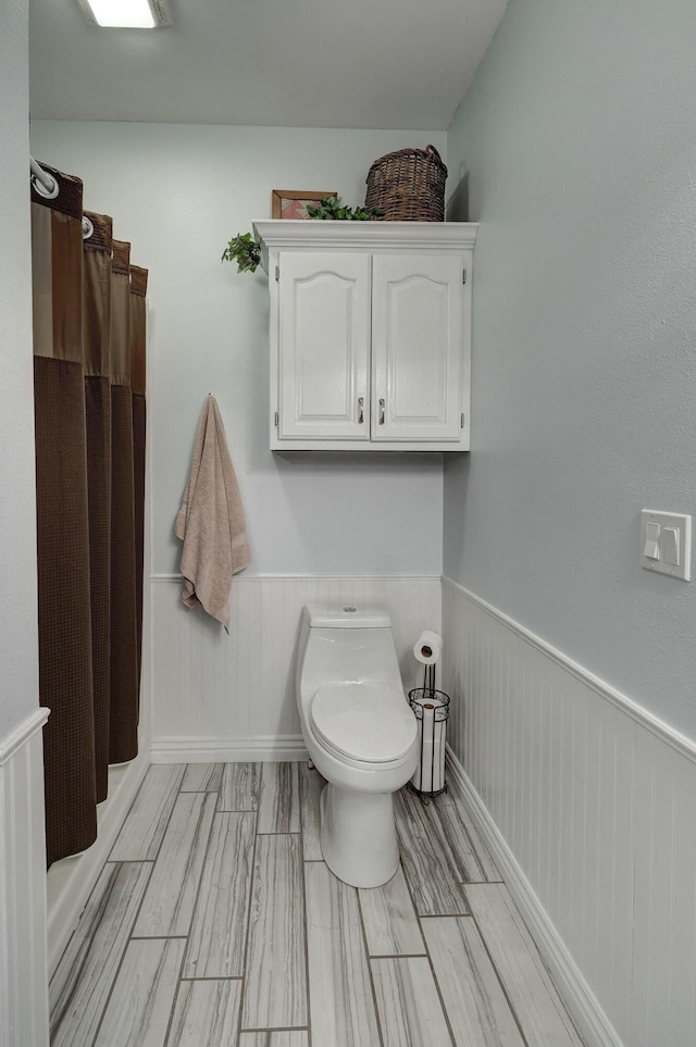 bathroom with wainscoting, curtained shower, and toilet