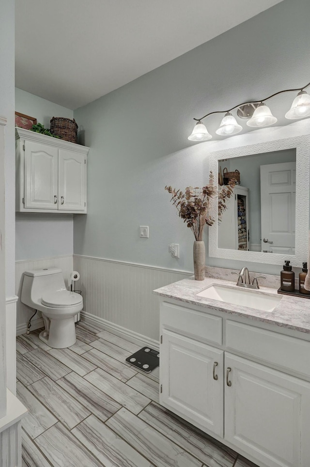 bathroom with vanity, toilet, and a wainscoted wall