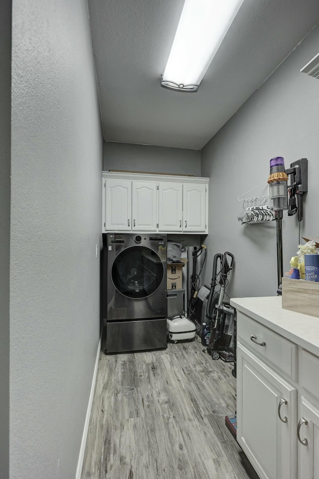 clothes washing area with baseboards, light wood-type flooring, washer / dryer, cabinet space, and a textured ceiling