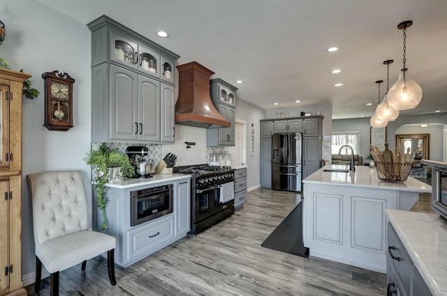 kitchen featuring gray cabinetry, a sink, custom range hood, glass insert cabinets, and appliances with stainless steel finishes