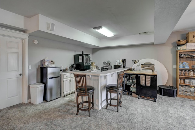 kitchen featuring a breakfast bar, a peninsula, freestanding refrigerator, and light carpet