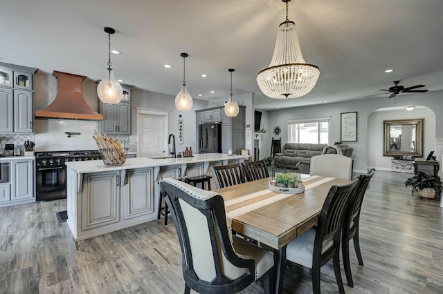 dining space with ceiling fan with notable chandelier, light wood-style flooring, recessed lighting, and arched walkways