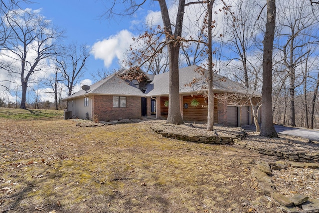 view of front facade featuring an attached garage, central AC unit, brick siding, and roof with shingles